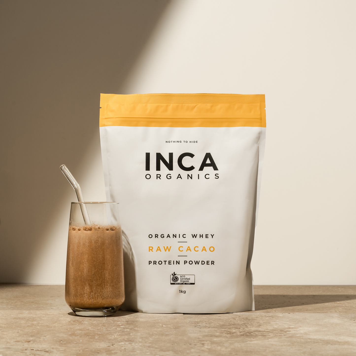 INCA Organics raw cacao protein powder bag with a glass of protein shake on a wooden surface.