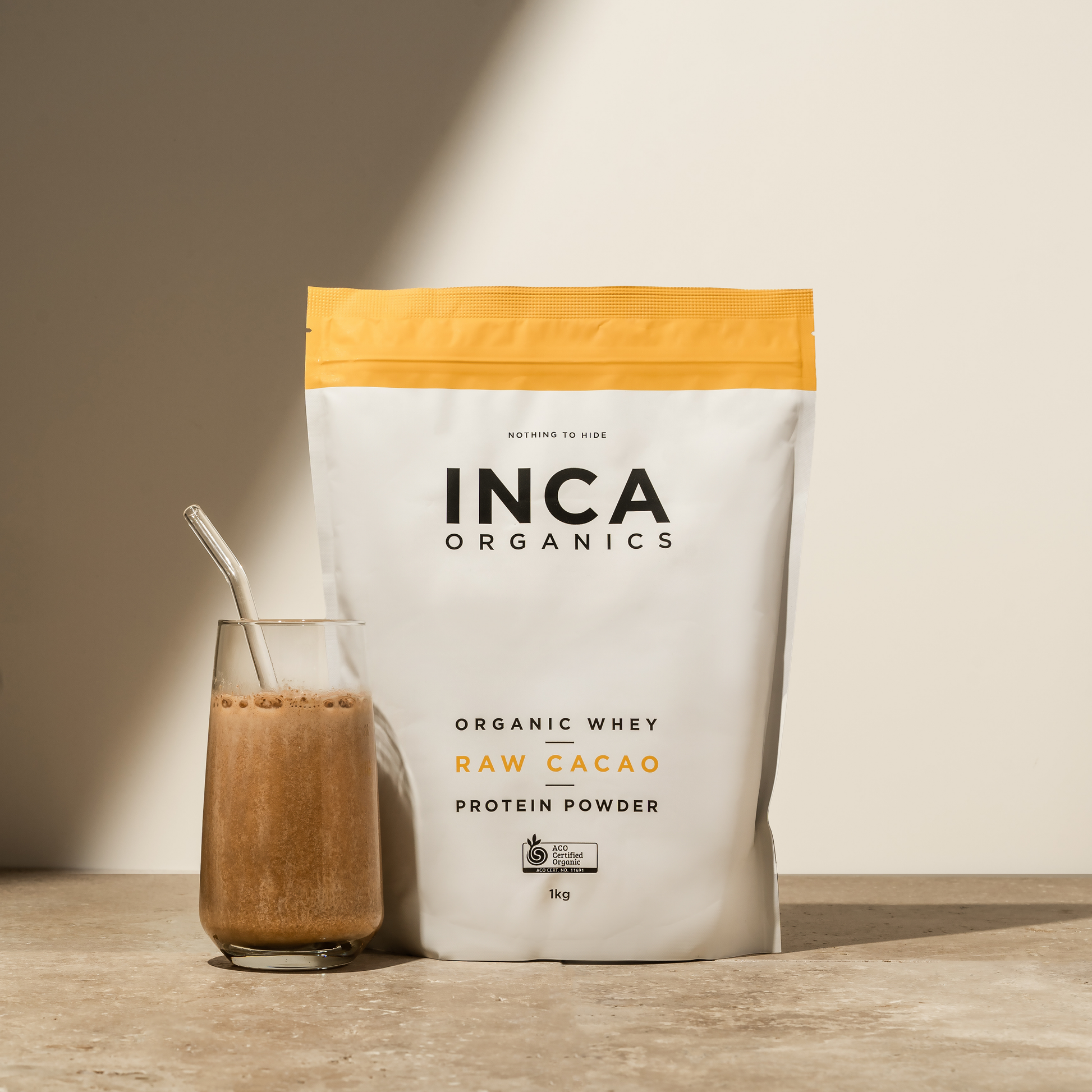 INCA Organics raw cacao protein powder bag with a glass of protein shake on a wooden surface.