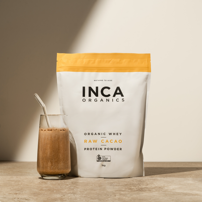 INCA Organics raw cacao protein powder bag with a glass of protein shake on a wooden surface.