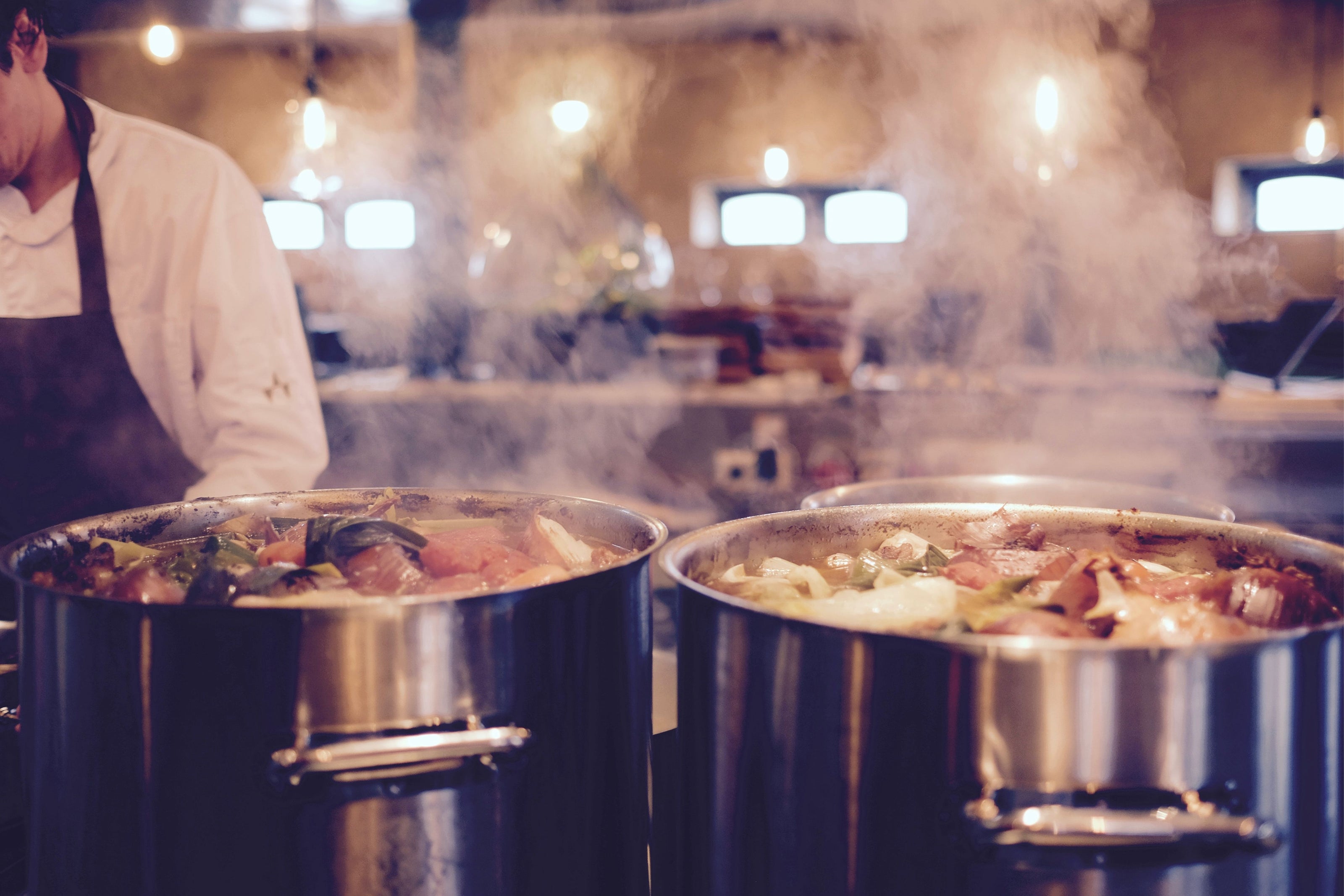 Two large pots of bone broth being simmered in a kitchen with steam rising.